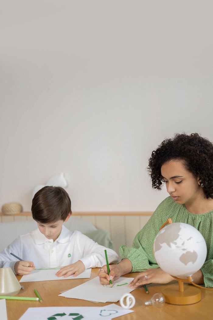 A woman and a boy draw with colored pencils and a globe in an eco-friendly classroom setting.