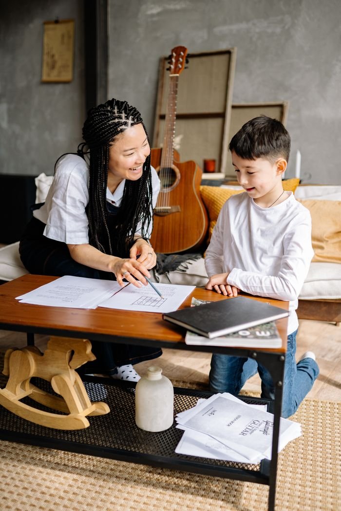 A woman teaching a young boy at a coffee table with papers and books, fostering learning and communication.